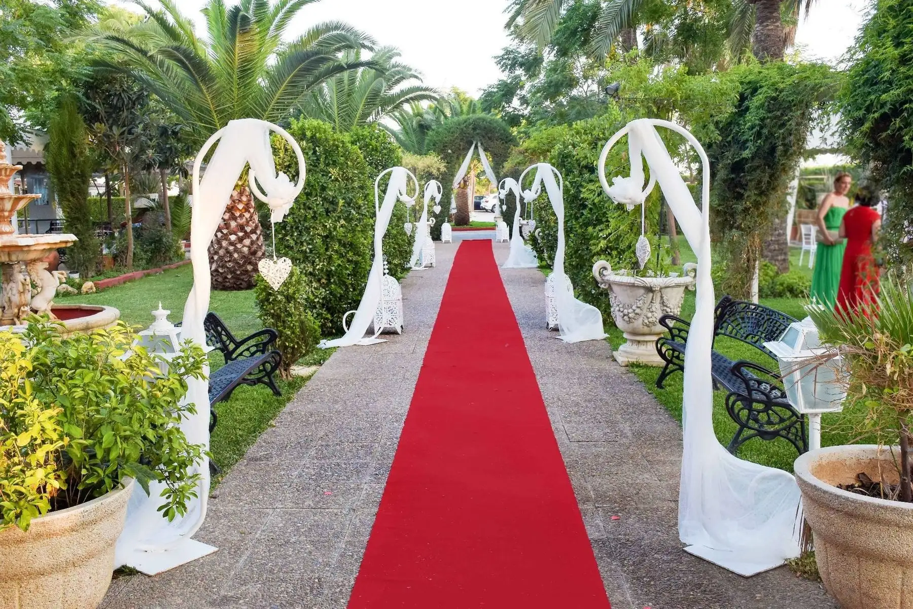 La alfombra roja entre setos, con lazos de tul blanco en arcos, lámparas marroquíes y una fuente al fondo