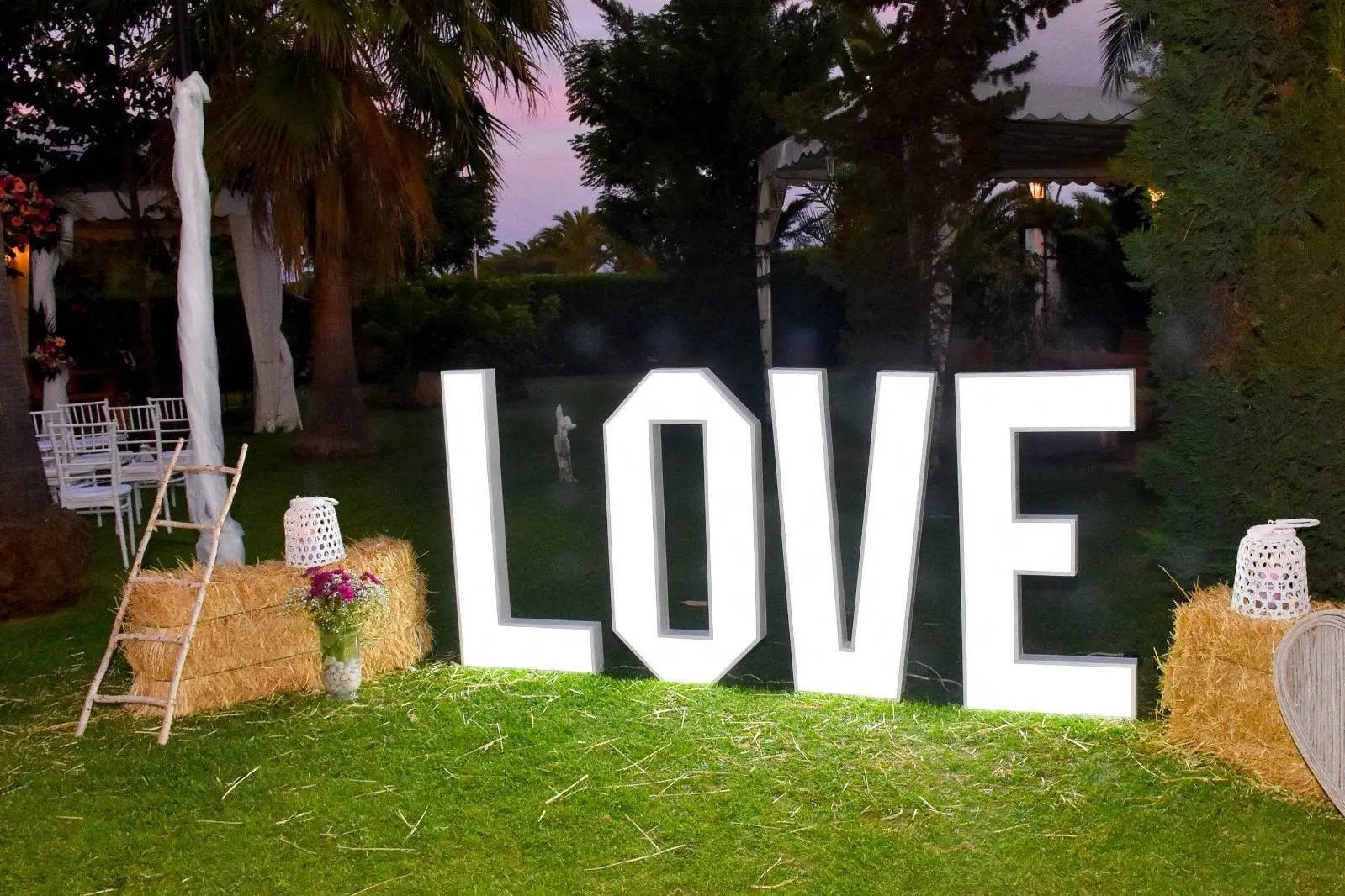 Las letras LOVE iluminadas sobre el césped al anochecer, con balas de paja
